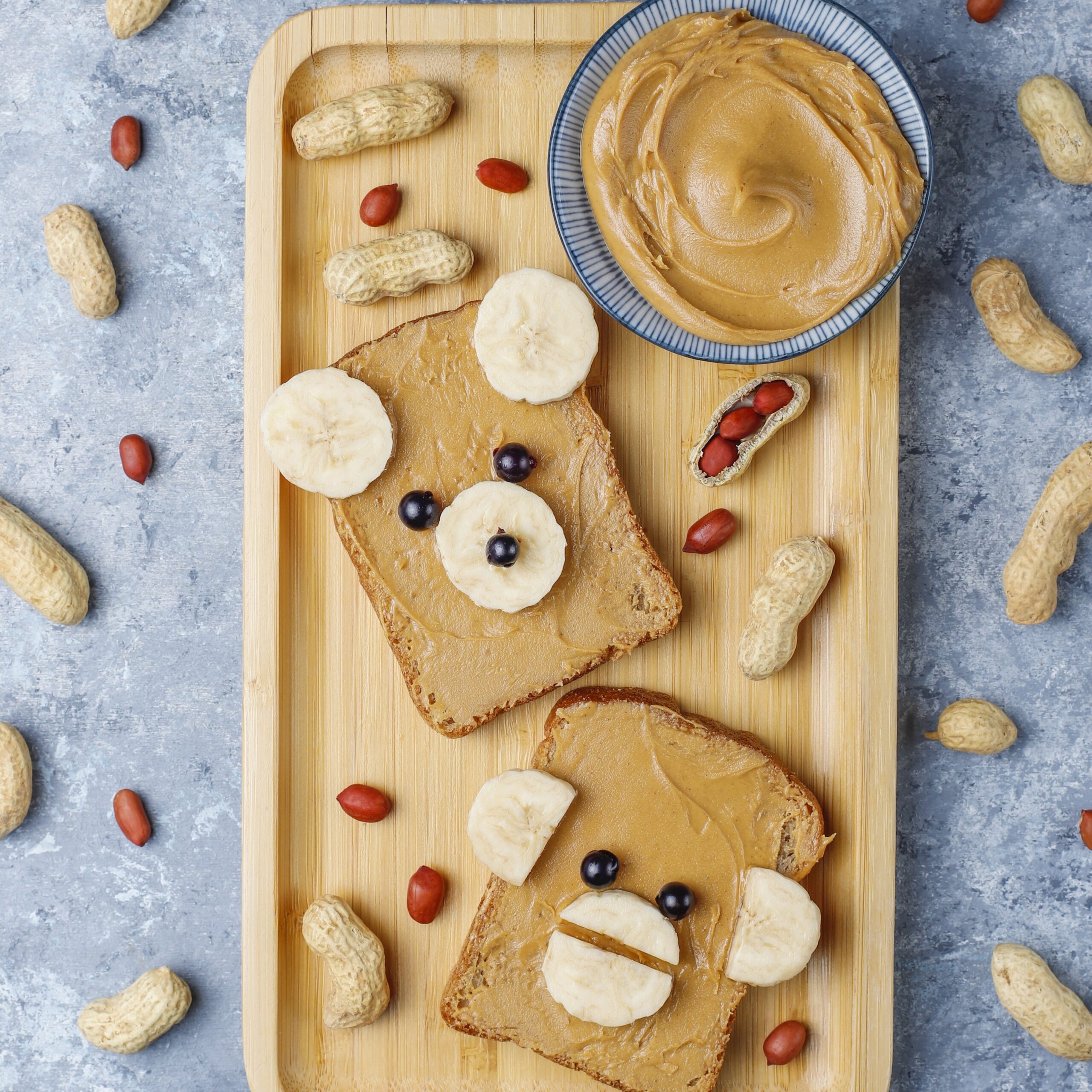 Funny bear and monkey face sandwich with peanut butter, banana and black currant,peanuts on grey concrete background,top view